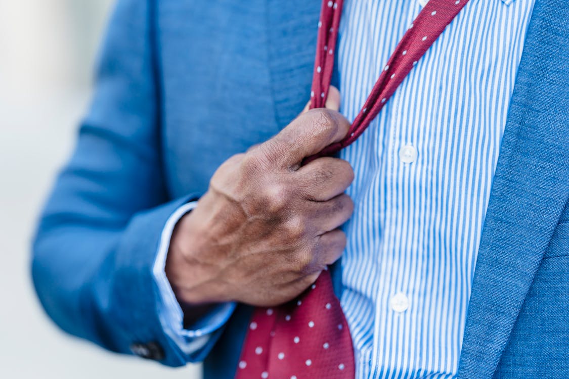 Free Crop anonymous tired male entrepreneur in formal suit adjusting red tie standing on street in city against blurred background after workday Stock Photo