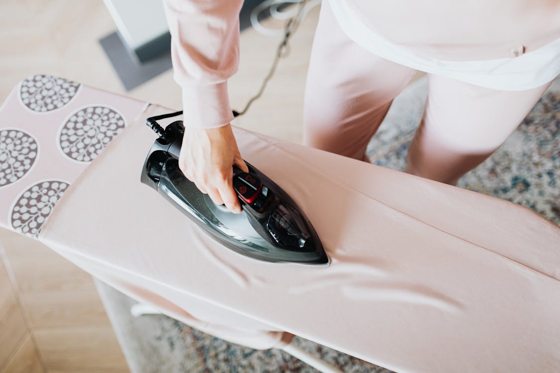 Free A person using a steam iron on a pink ironing board indoors, focusing on household chores. Stock Photo