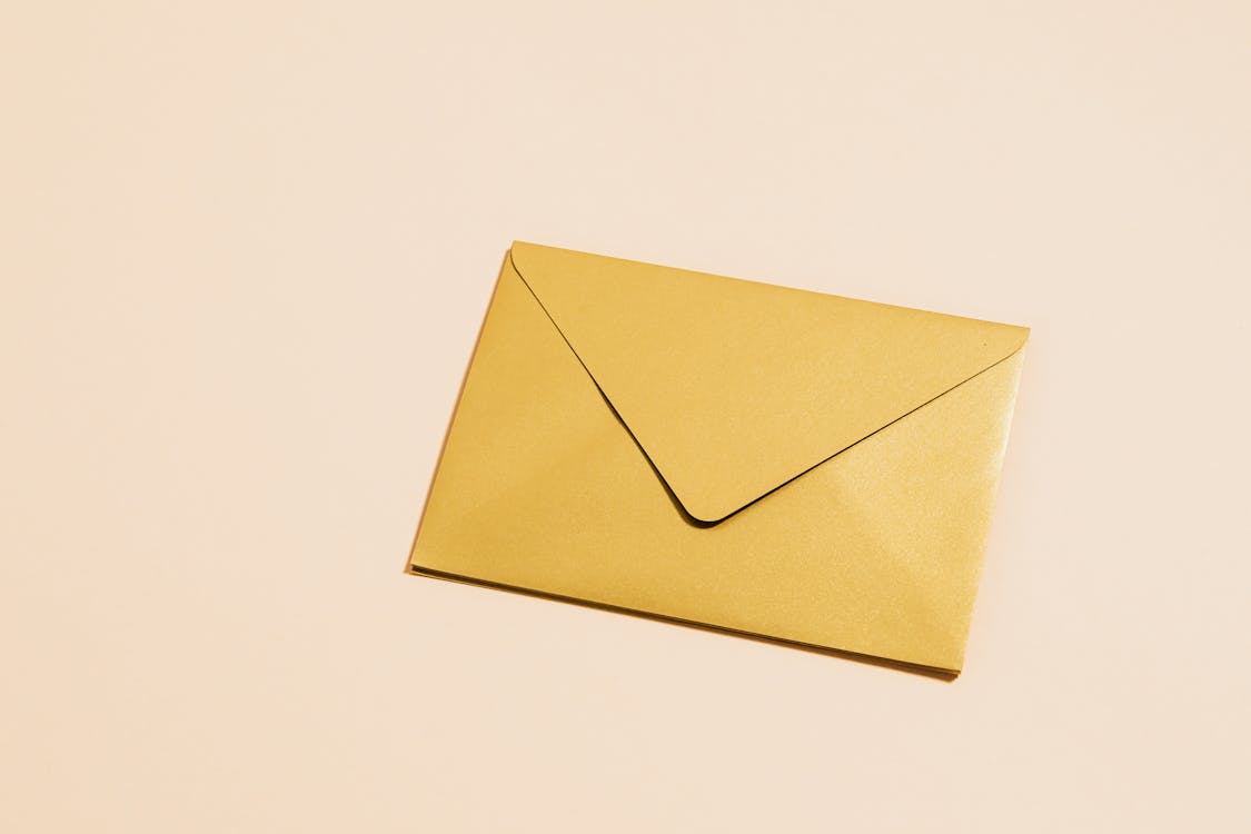 Free A sleek gold envelope placed on a vibrant yellow background, perfect for postal themes. Stock Photo