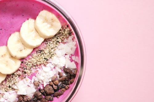 Free A brightly colored smoothie bowl with fresh banana, seeds, and coconut flakes on a pink background. Stock Photo